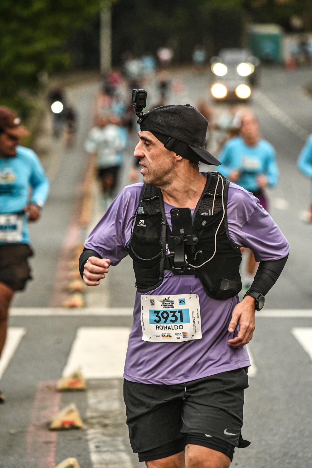 Corredor de camiseta roxa, colete de hidratação Salomon e boné correndo os 21k da Maratona Internacional de Blumenau, número 3931, com câmera GoPro na cabeça